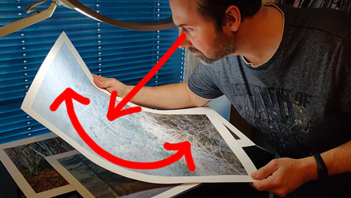 Photographer examining printed photographs with red arrows indicating comparison between prints.