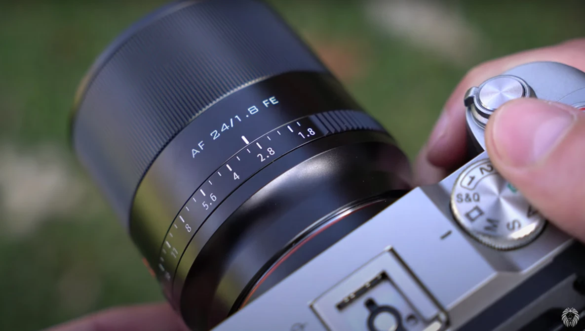 Close-up of a rangefinder camera lens showing AF 2.8/28mm focal length marking and aperture ring being adjusted by a photographer's hand.