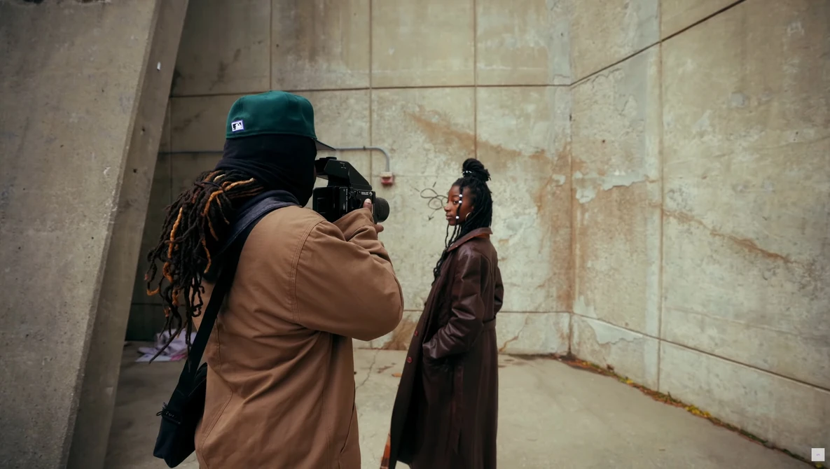Photographer with camera and backpack captures portrait of woman in concrete stairwell.