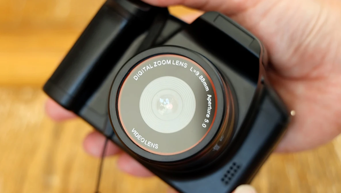 Hand holding a compact digital camera with a digital zoom lens, displaying the lens barrel and front glass element.