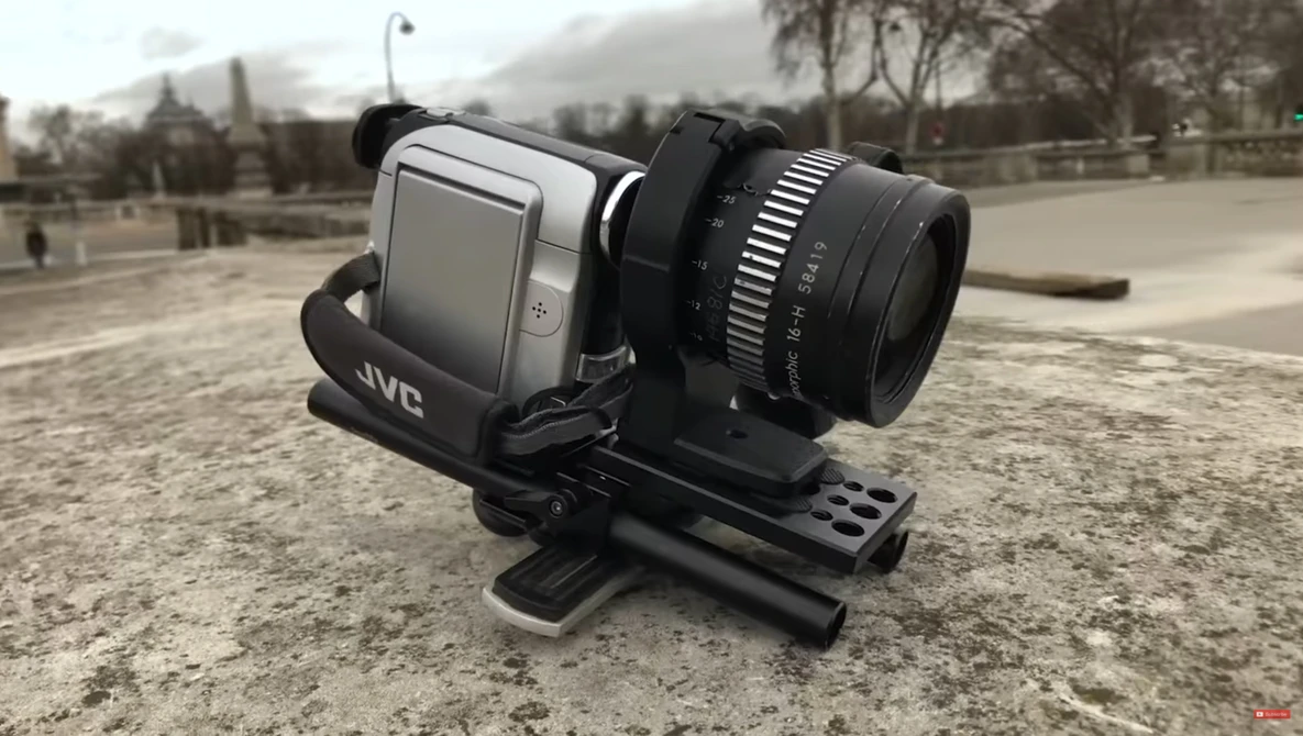 JVC compact camcorder mounted on a stabilizing rig with external lens attachment, positioned on ground-level support.