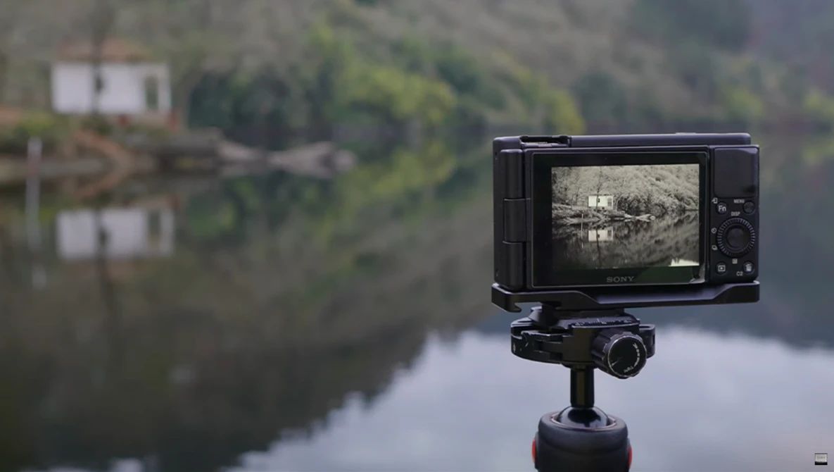 External monitor mounted on tripod displaying live footage of a misty lake landscape with forested shoreline.