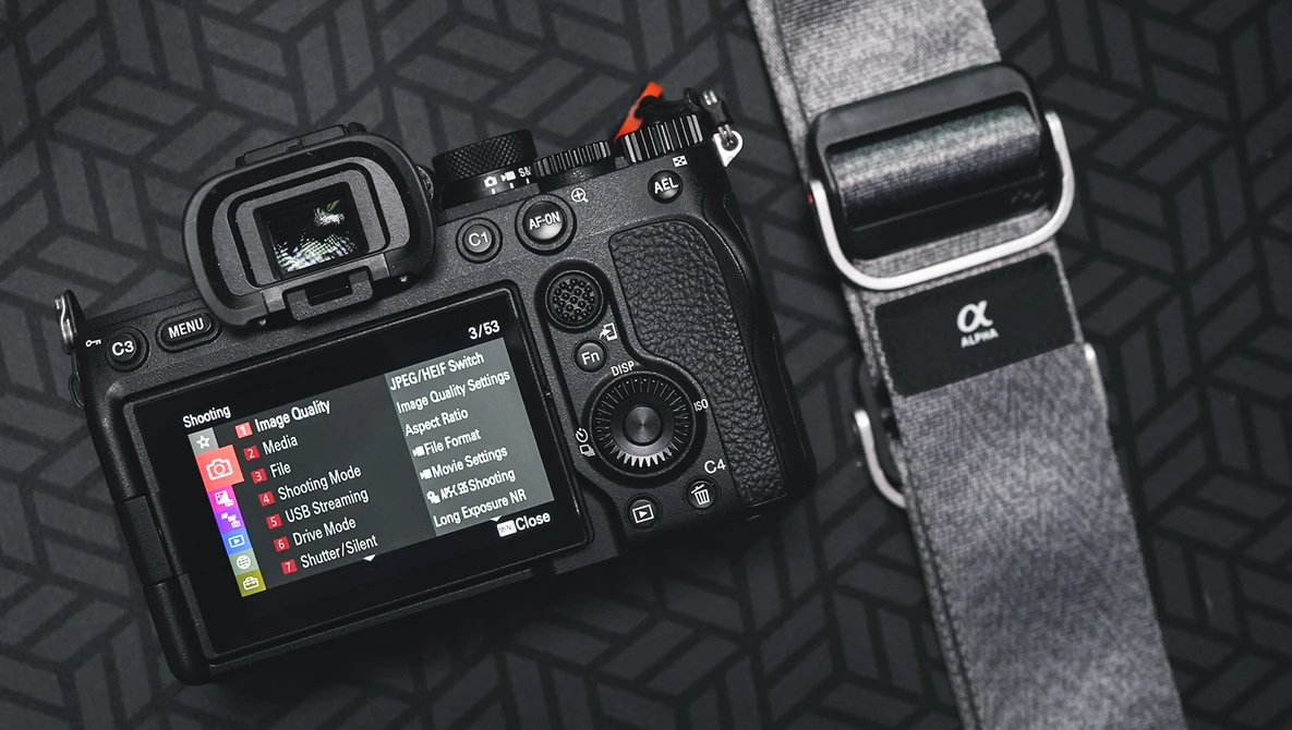 Sony Alpha mirrorless camera displaying menu screen alongside camera strap on geometric patterned surface.