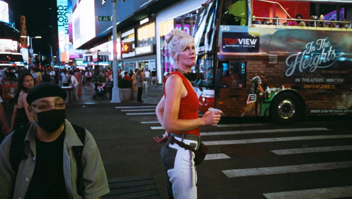 Jogger in red tank top and white pants running across a crosswalk in a busy urban theater district at night.