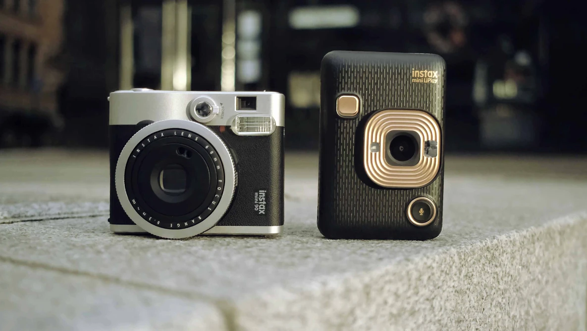 Two vintage instant cameras displayed side by side on a concrete surface.