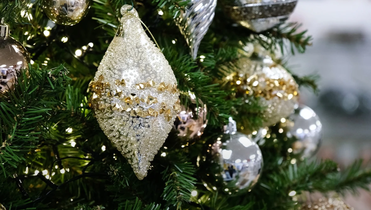 Gold and silver glittered teardrop ornaments hanging from evergreen branches with soft bokeh background.