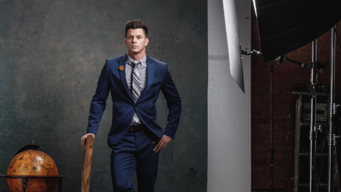 Man in navy blazer and striped tie standing in studio with globe and industrial backdrop.