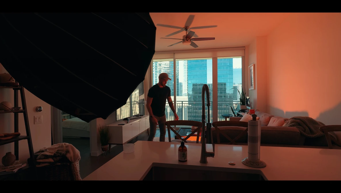 Studio interior with warm orange-toned lighting, featuring a person standing near large windows overlooking a city skyline.
