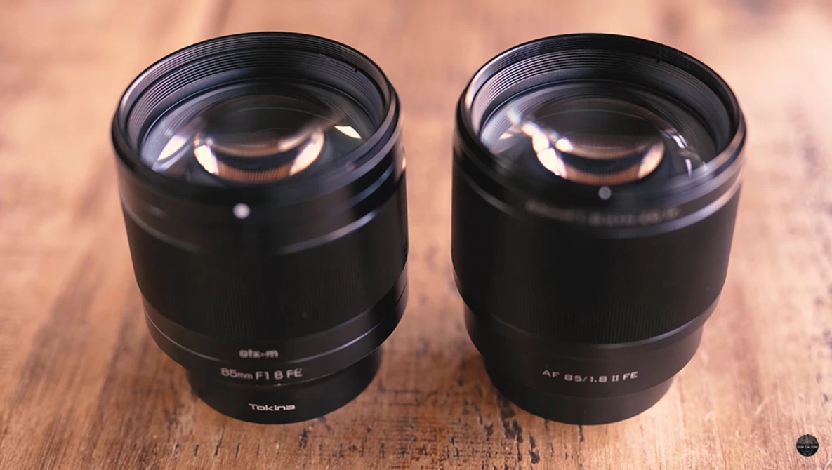 Two black telephoto lenses with large front elements positioned side by side on a wooden surface.