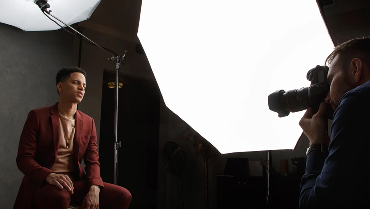 Photographer shooting a portrait of a man in a burgundy suit in a studio setting with softbox lighting.