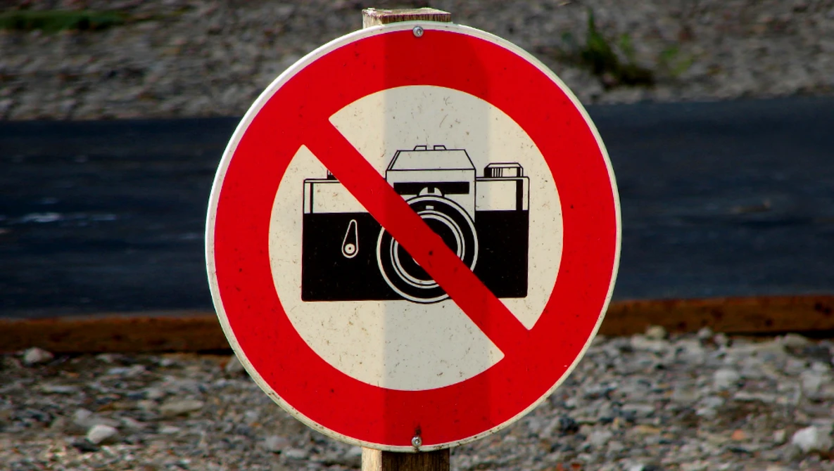 Red and white prohibition sign with a camera crossed out by a diagonal line.