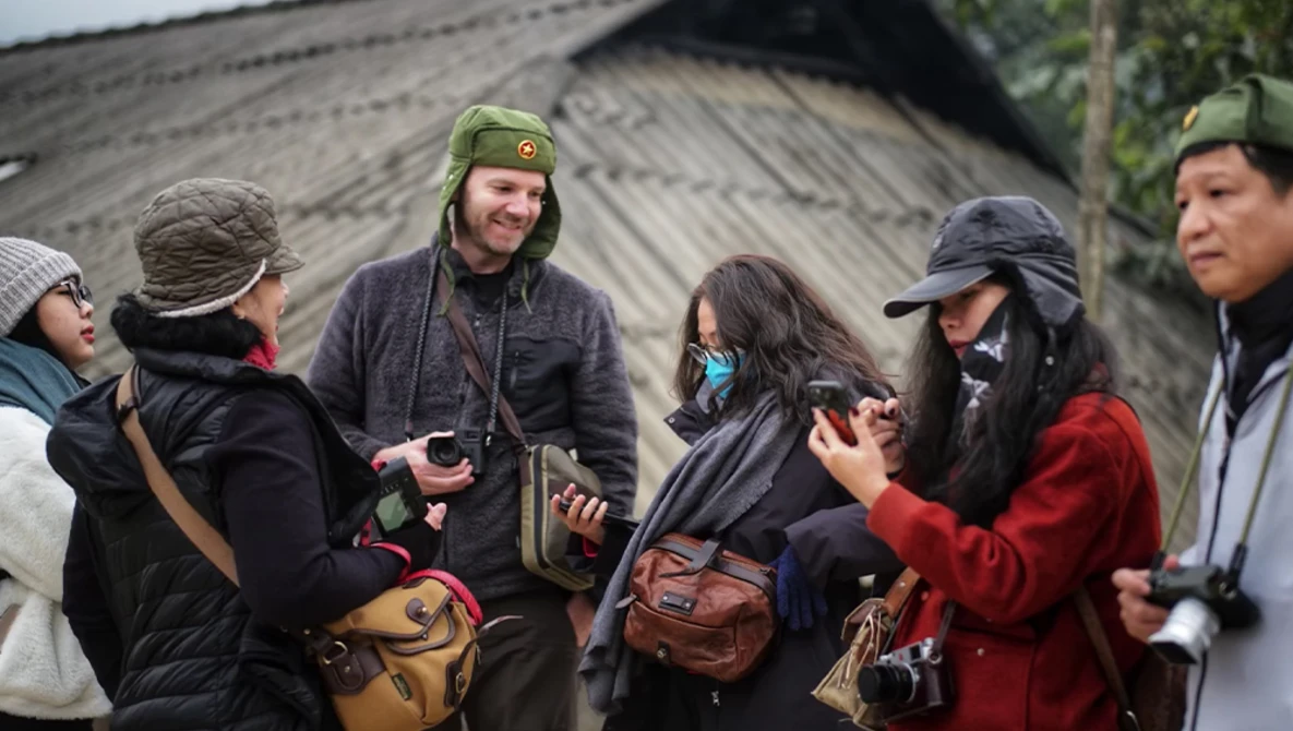 Group of five people wearing winter clothing and caps gathered outdoors, engaged in conversation.