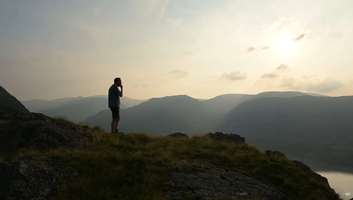 Silhouetted hiker standing on a rocky outcrop overlooking a misty mountain valley at sunset.