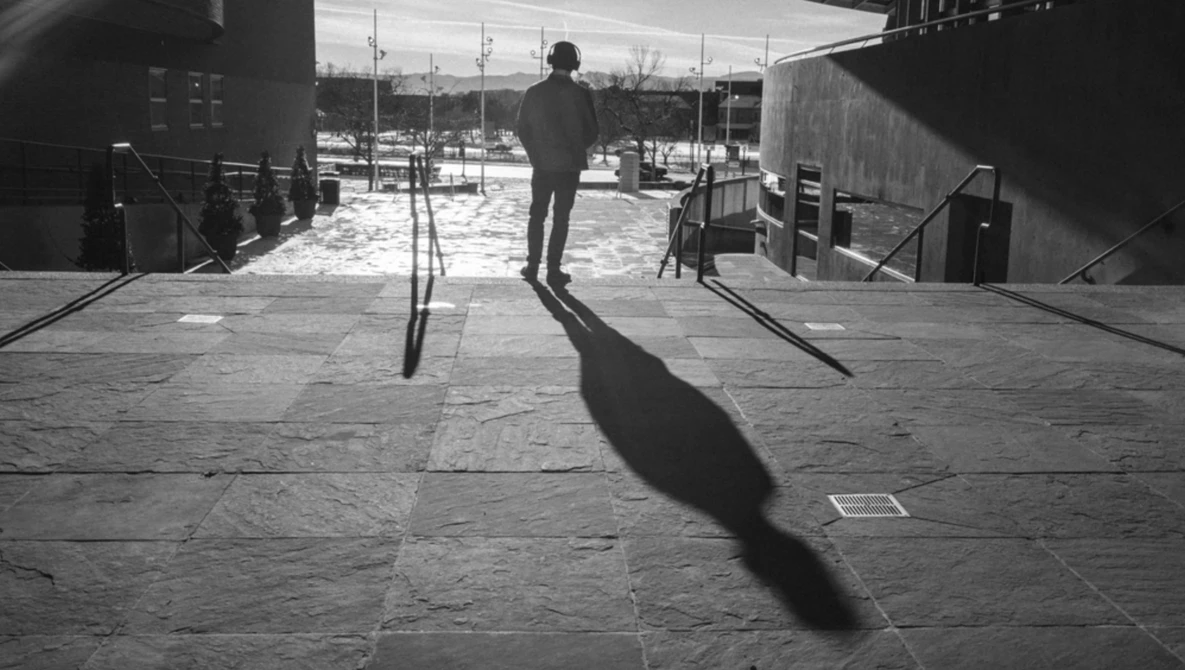 Silhouetted figure standing on a concrete plaza with a dramatic shadow cast across the ground.