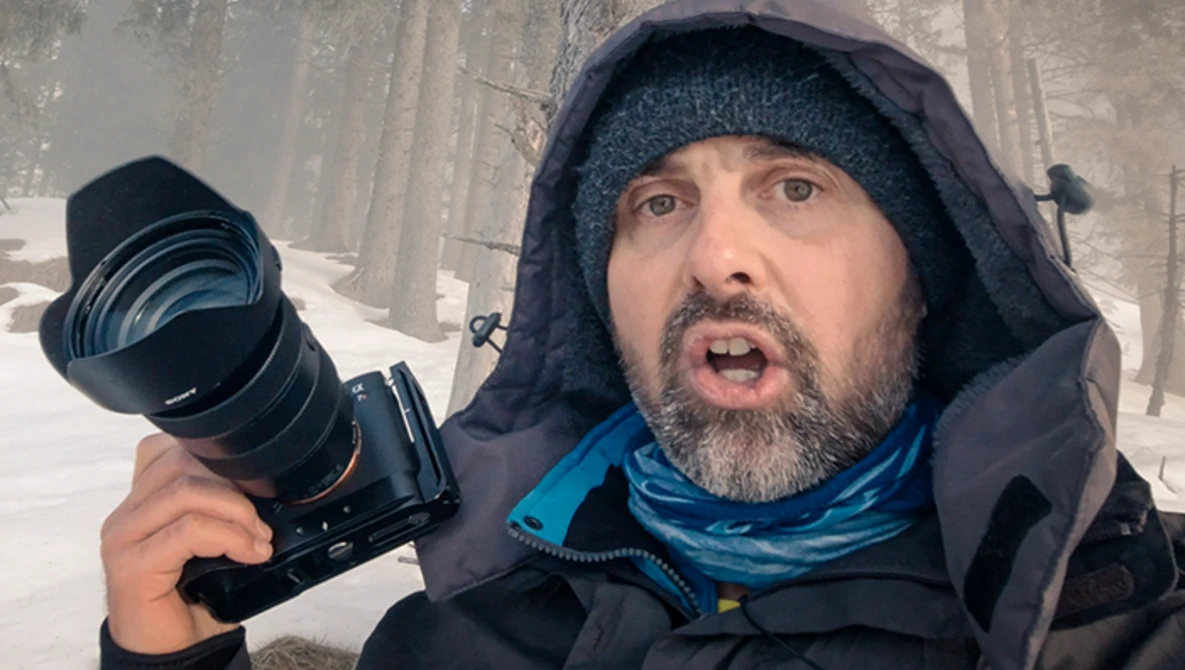 Photographer holding a telephoto lens in snowy conditions while wearing winter gear.