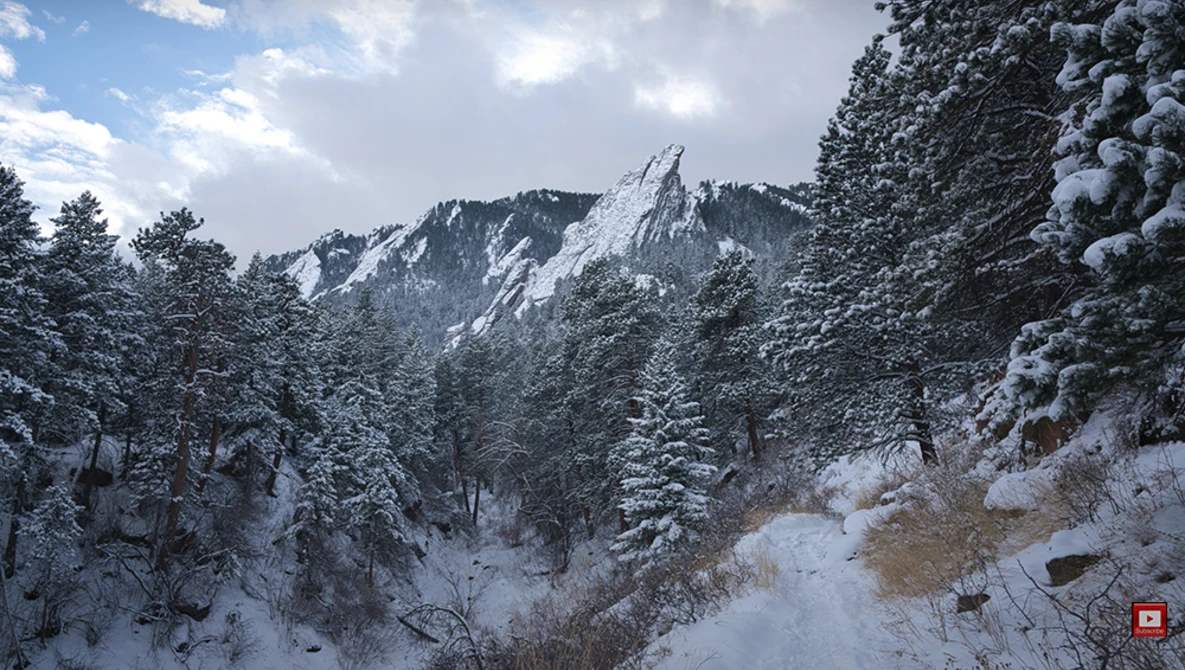 Snow-covered evergreen forest with a rocky mountain peak rising through the trees under partly cloudy sky.
