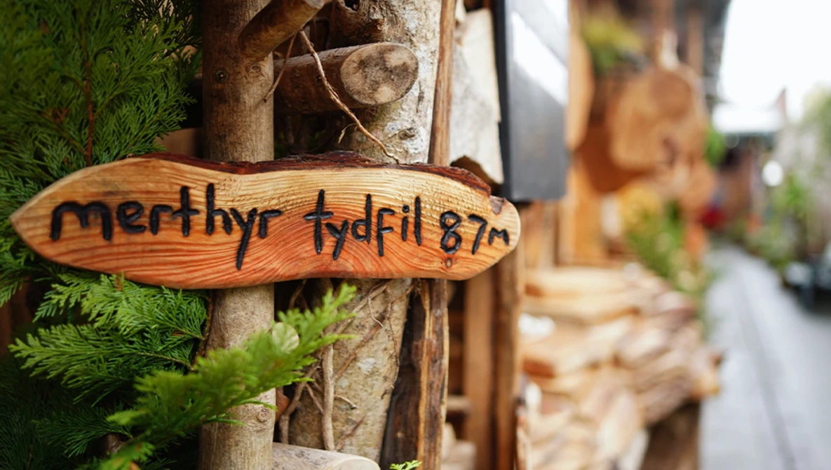 Wooden engraved nameplate reading "merthyr tydfil 67" attached to a weathered post or tree trunk.