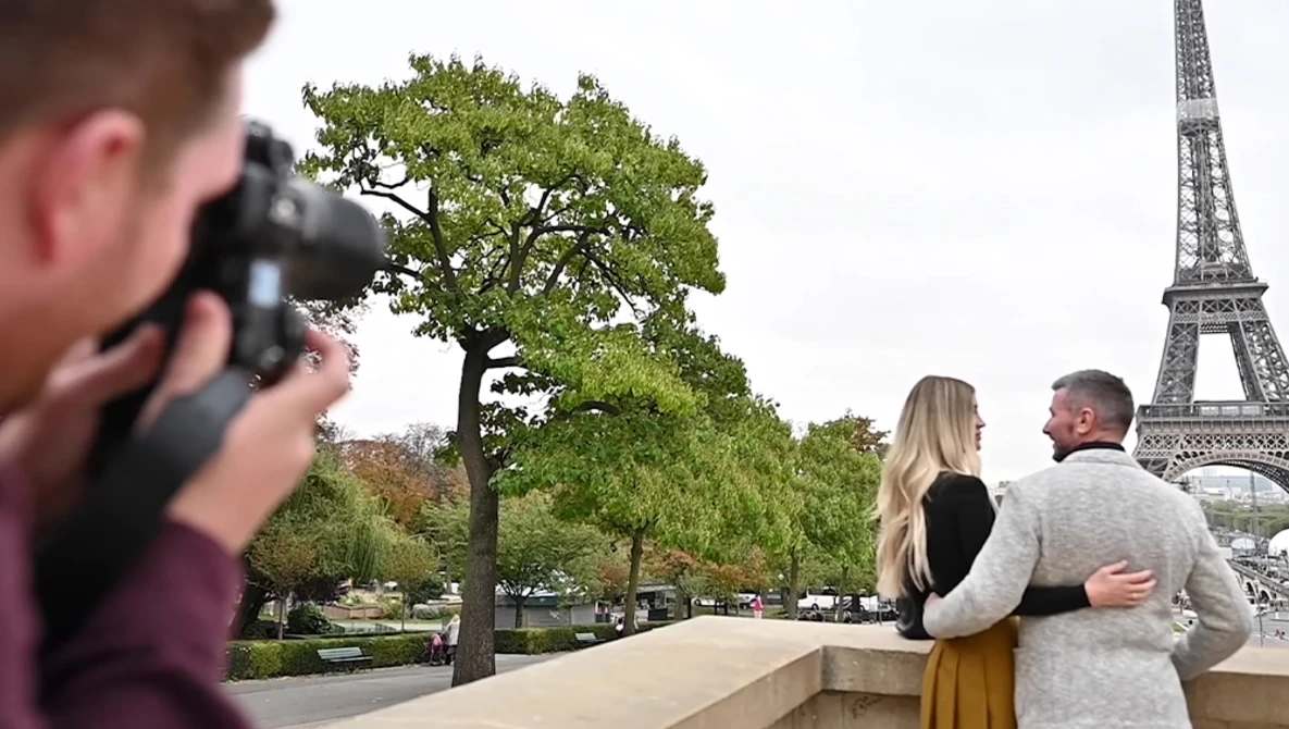 Photographer capturing a couple posing together with an iconic iron tower in the background.