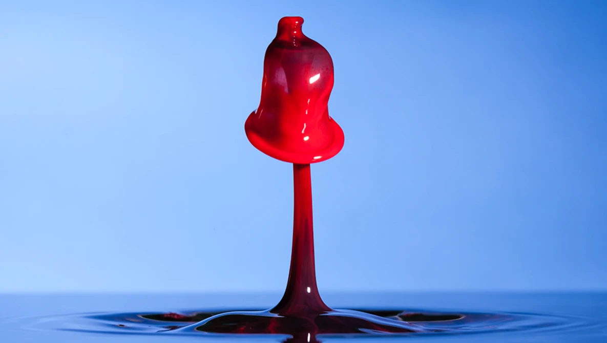 Red liquid drop suspended above water surface against blue background.