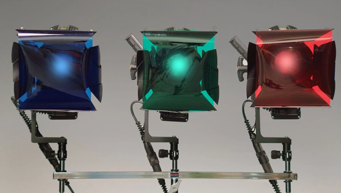 Three professional LED panel lights mounted on a horizontal rig, each emitting different colored light: blue, green, and red.