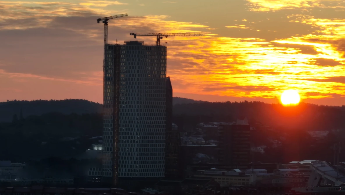 Tall residential tower under construction at golden hour, silhouetted against dramatic sunset sky with construction cranes visible at top.