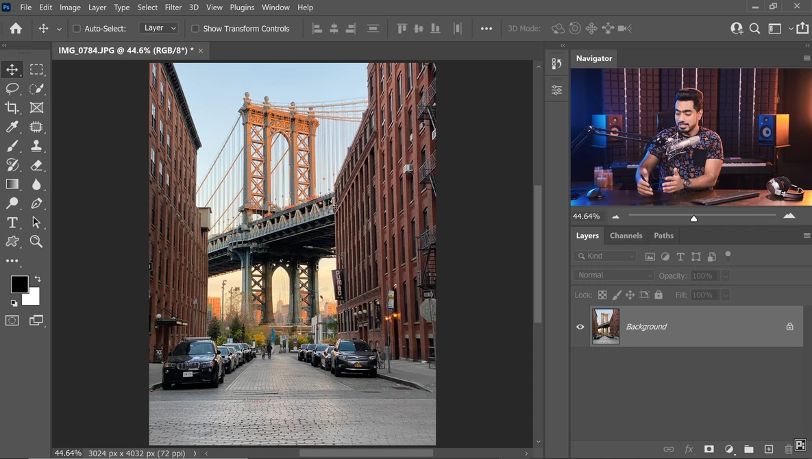 Urban street lined with brick buildings frames a suspension bridge in warm golden light.