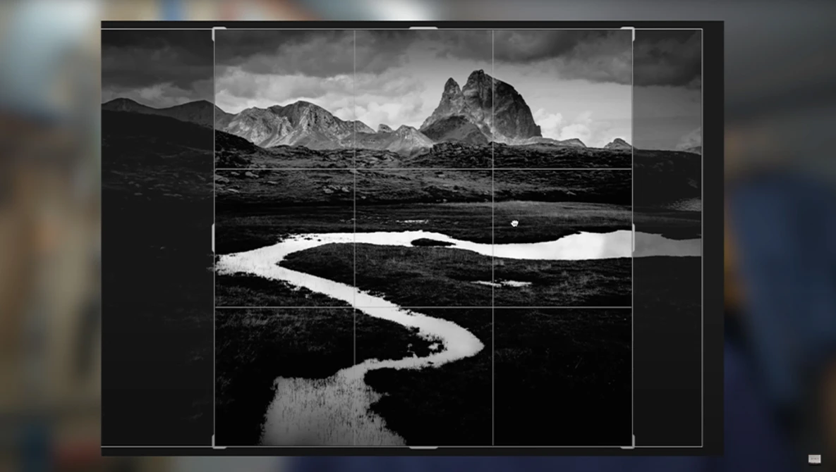 Black and white landscape with a winding river through dark terrain and dramatic mountains under stormy sky, divided by rule-of-thirds grid overlay.