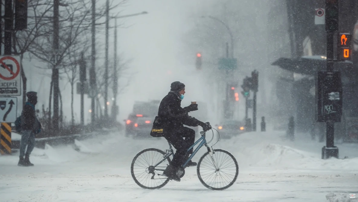 Cyclist riding through heavy snow on an urban street during a blizzard.