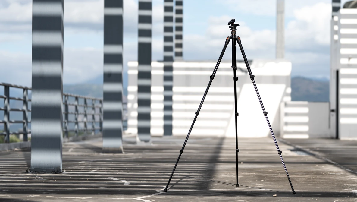 Camera tripod set up on a rooftop with modern skyscrapers and mountains in the background.
