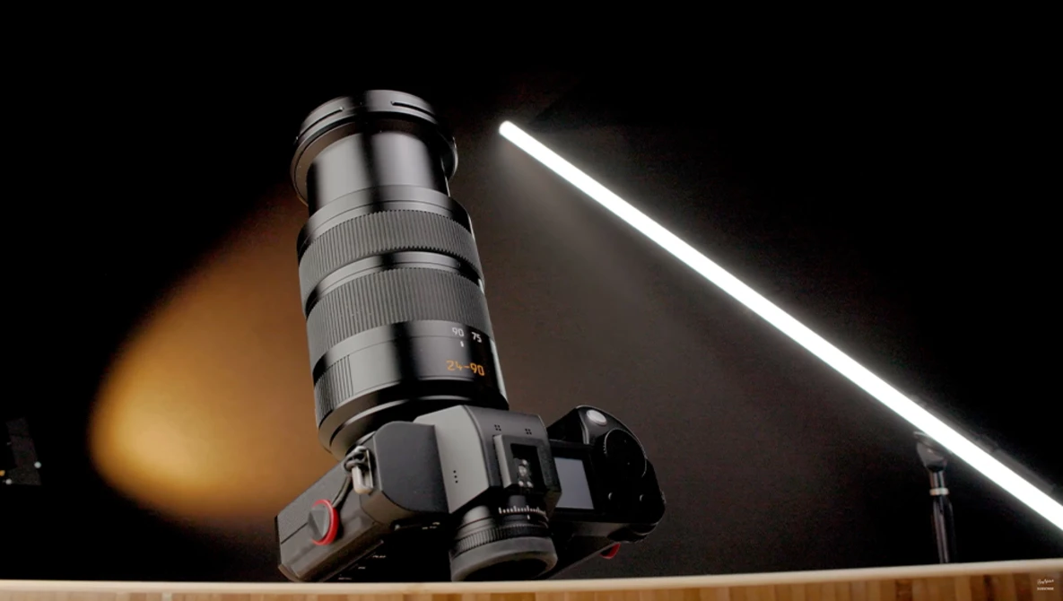 Telephoto lens mounted on camera body with studio lighting setup against black background.