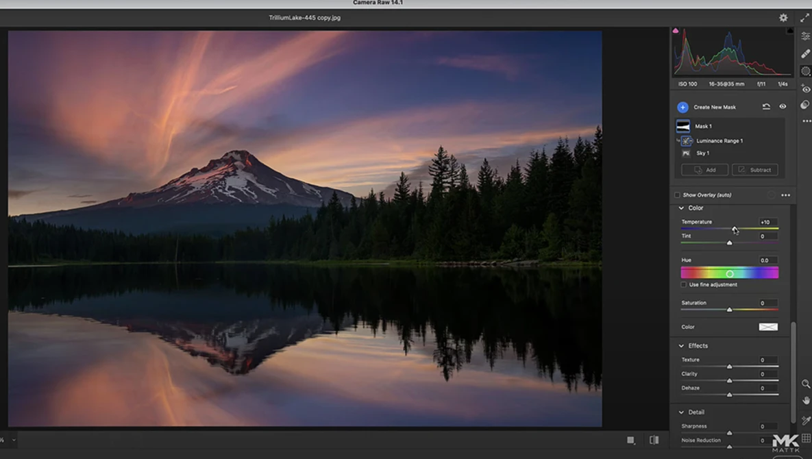 Snow-capped volcanic mountain reflected in still lake at sunset with forest silhouette.