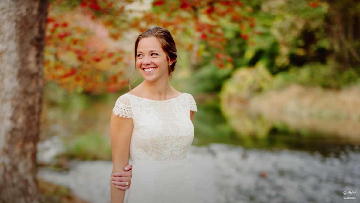 Woman in white lace dress smiling beside tree with ivy and red berries.