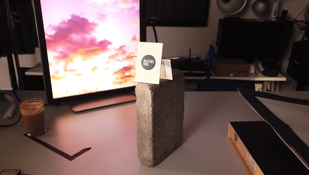 Concrete block with white label on studio desk displaying colorful sunset sky on monitor.
