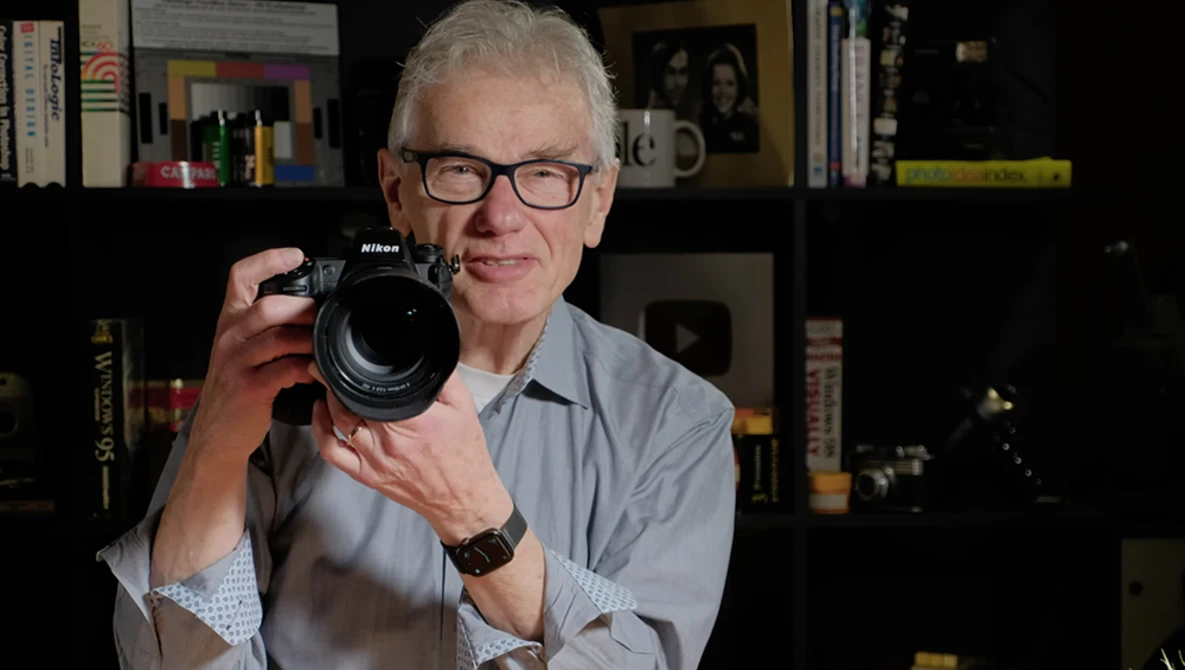 Photographer holding a Nikon DSLR camera with lens extended toward the camera.