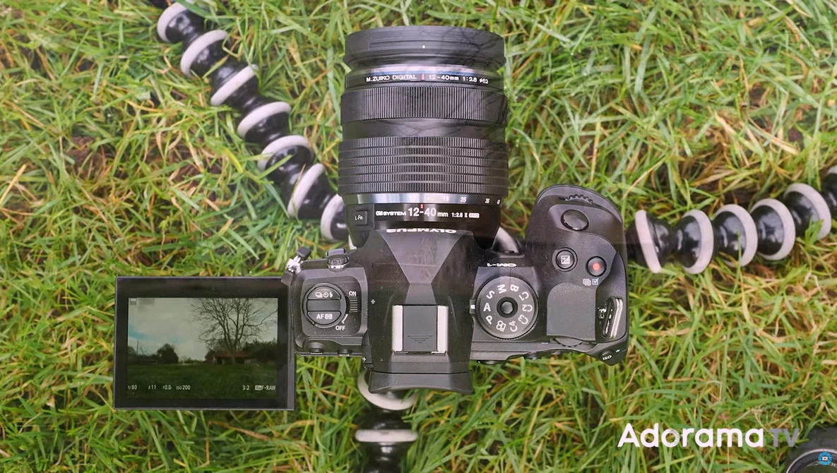 Camera gear laid out on grass including a DSLR body, telephoto lens, external flash, and various lens attachments.