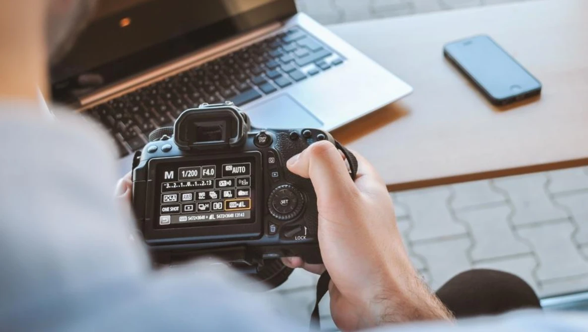 Photographer holding DSLR camera displaying rear LCD screen with menu settings visible.