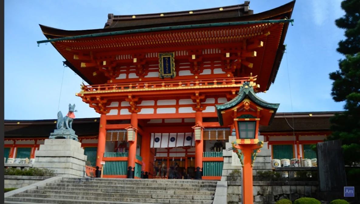 Bright red traditional Japanese temple gate with ornate curved roofing and golden accents under clear blue sky.