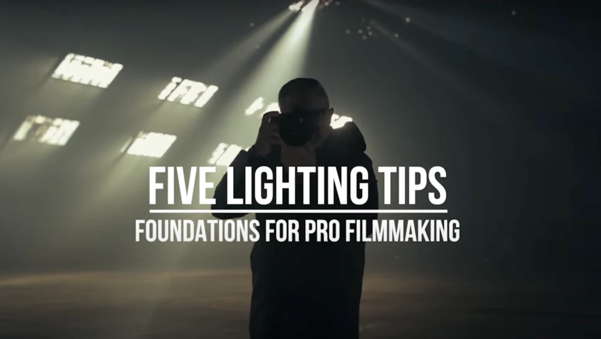 Silhouetted figure backlit by studio lights casting dramatic shadows. Title card reads 'Five Lighting Tips: Foundations for Pro Filmmaking.'