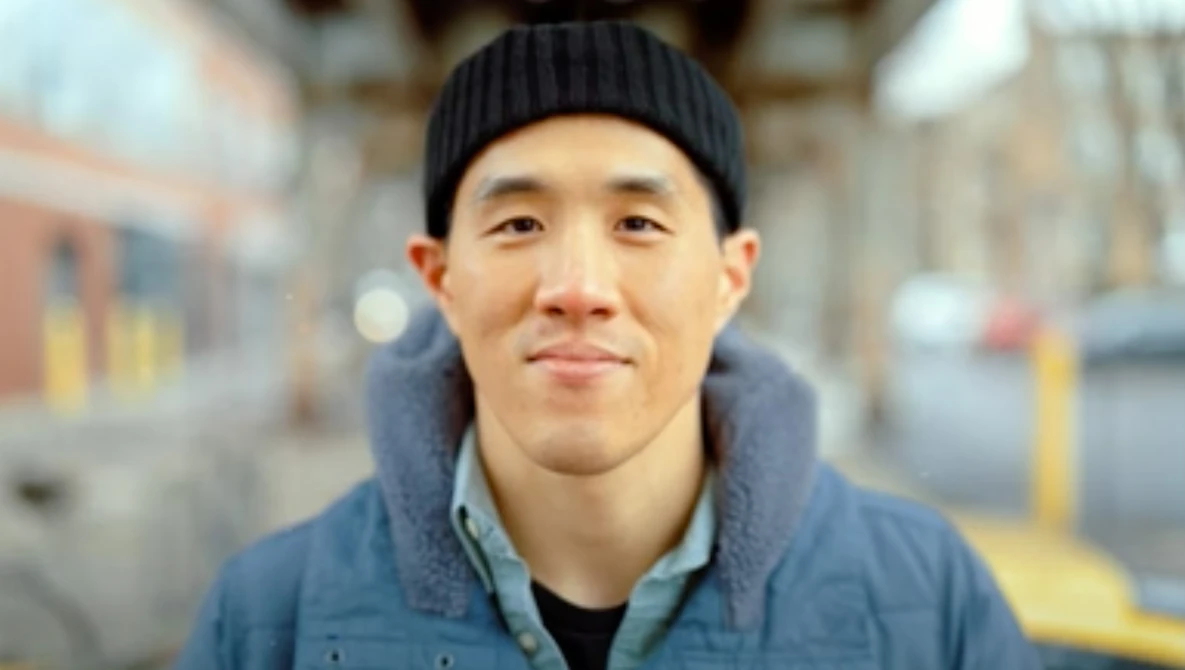 Portrait of a man wearing a black beanie and blue jacket against a blurred urban street background.