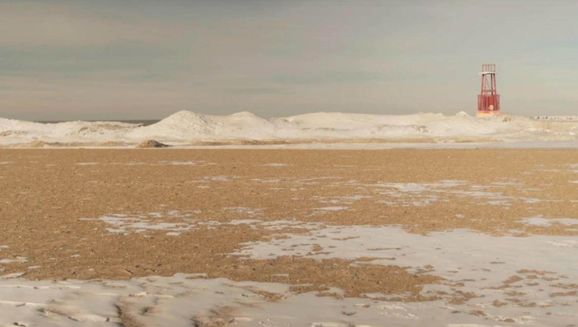 Frozen lake with industrial salt mounds and red navigation tower in winter landscape.