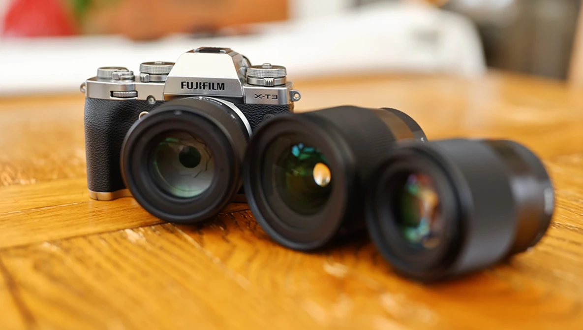 Fujifilm X-T5 camera with three interchangeable lenses arranged on wooden surface.