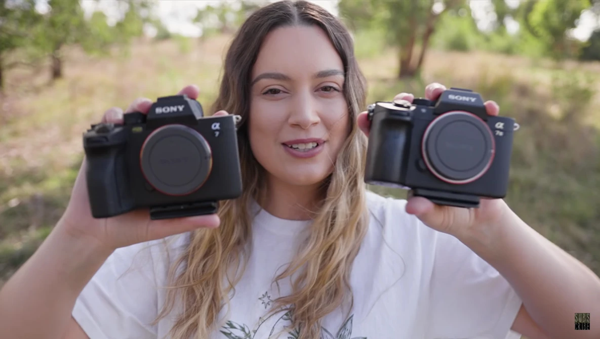 Photographer holding two Sony Alpha mirrorless cameras side-by-side outdoors.