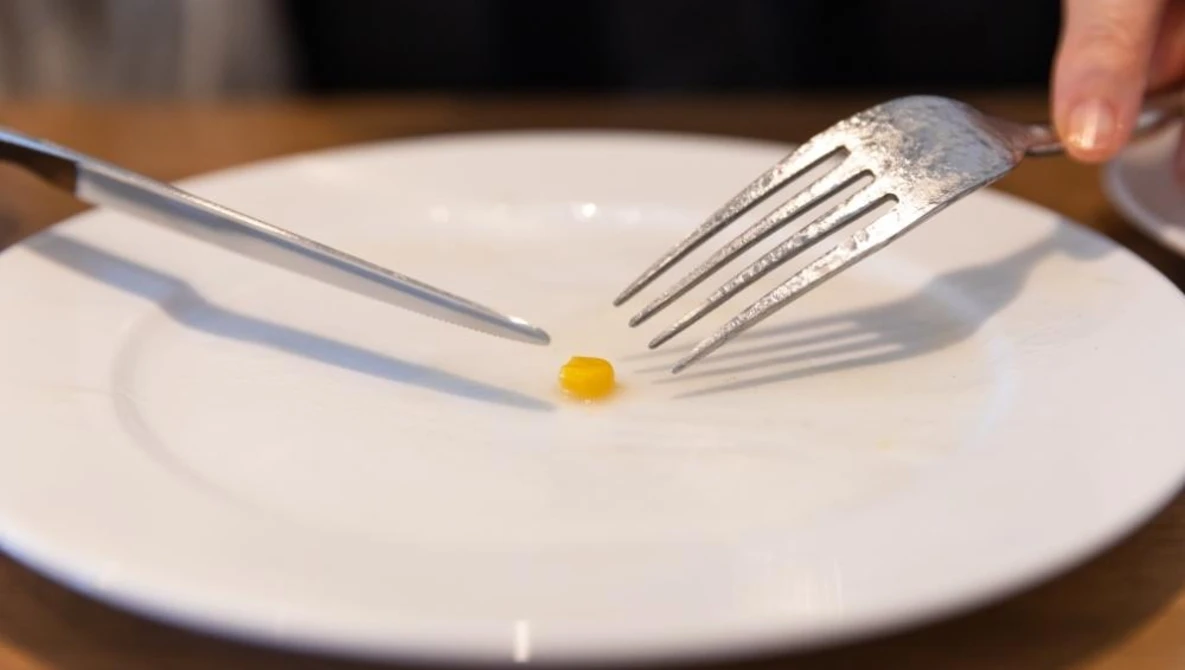 Fine dining plating technique with a single quail egg centered on a white plate, positioned between fork and knife.
