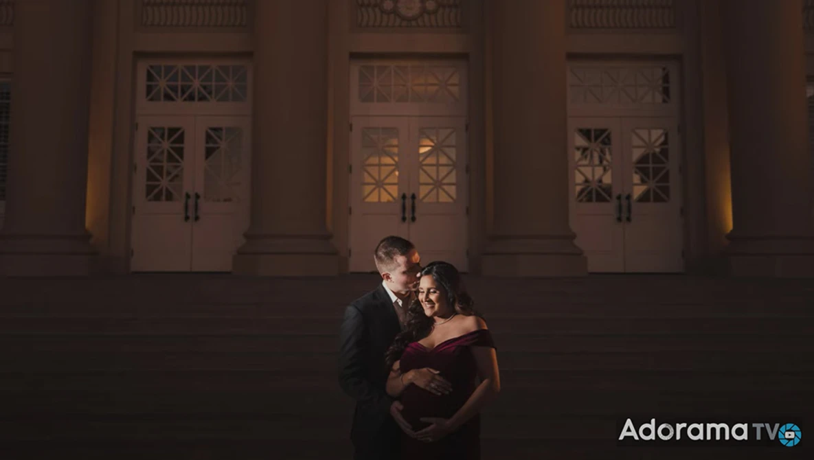Couple embracing in front of an ornate building entrance at night with warm uplighting.