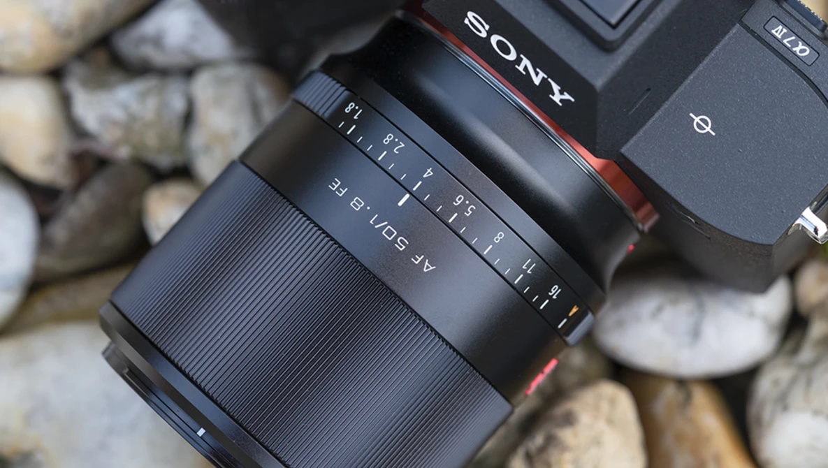 Sony lens with focus ring and aperture markings mounted on camera body, shot on textured stone surface.