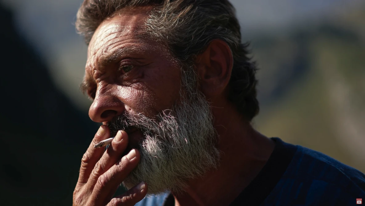 Bearded man in profile with hand near mouth, backlit by soft natural light.