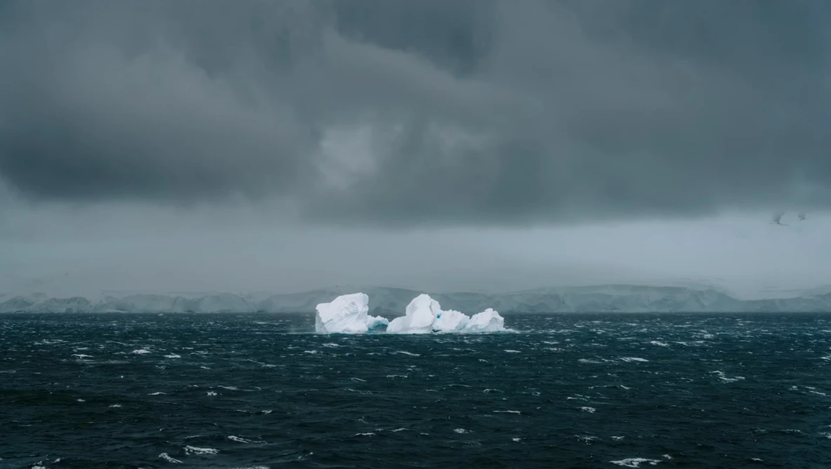 Icebergs floating in dark, choppy ocean waters beneath stormy gray clouds.
