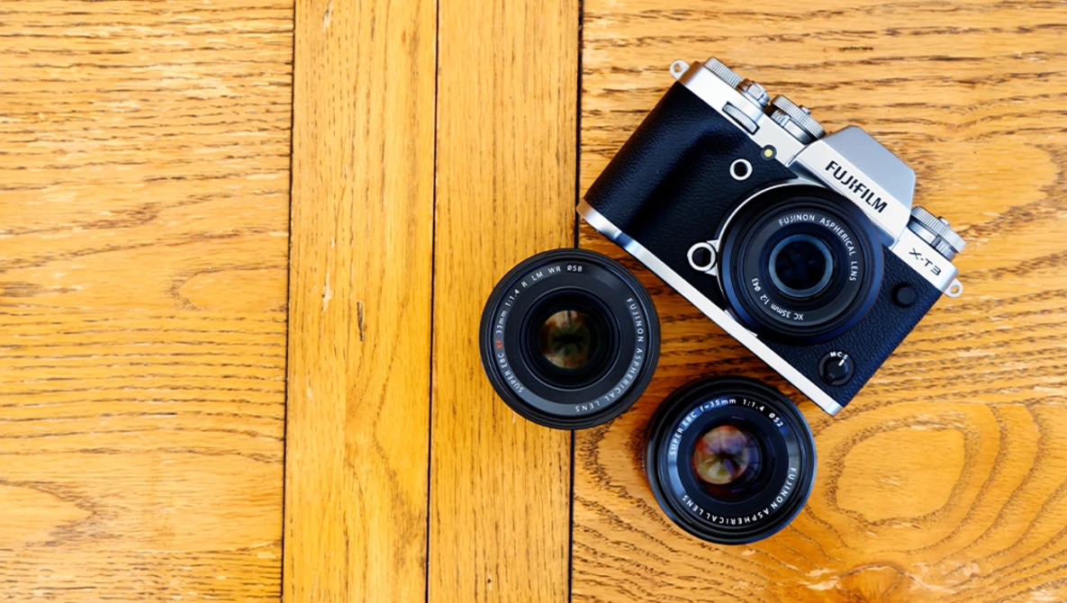 Fujifilm rangefinder camera with two interchangeable lenses on wooden surface.