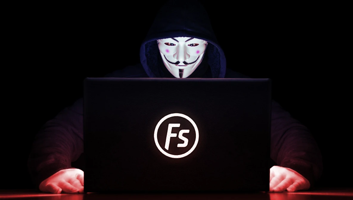 Figure wearing Guy Fawkes mask at laptop displaying FS logo in dark setting.