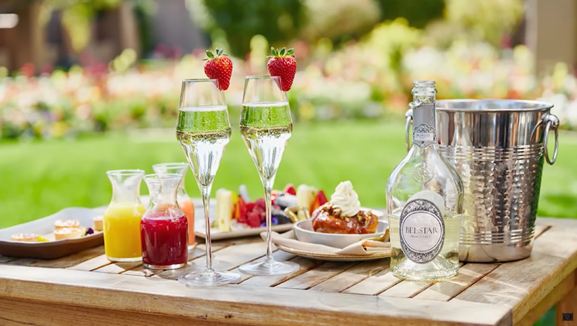 Outdoor garden table set with champagne flutes, strawberries, juice glasses, and a bottle in an ice bucket.